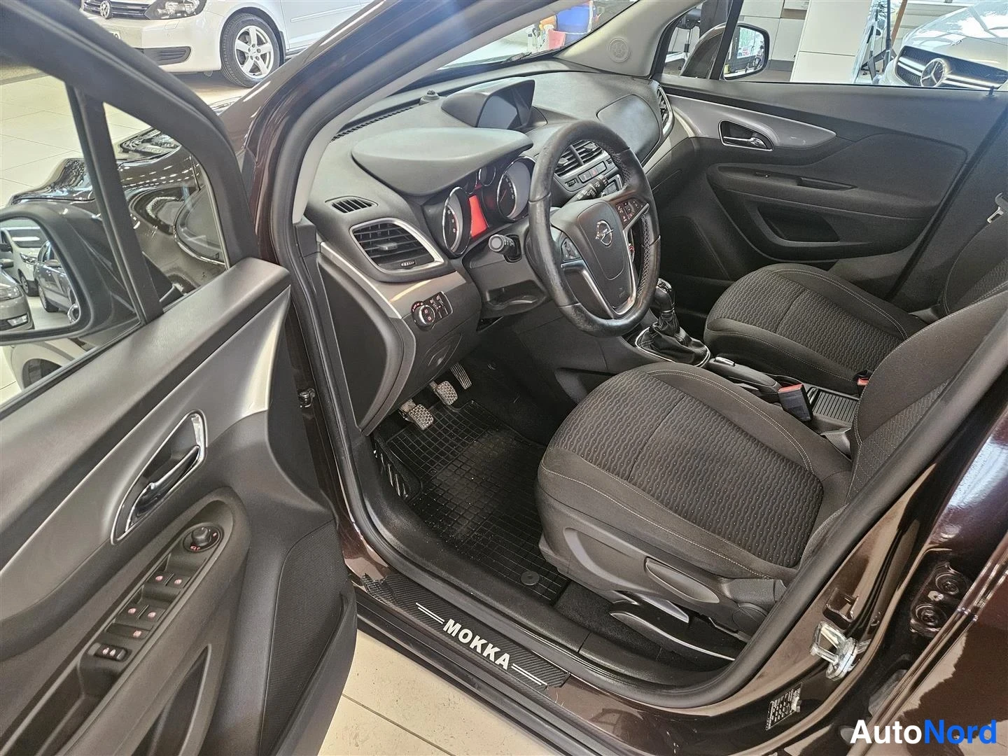 Muu: Kuljettajan puolen ovi auki: tumma sisusta, Opel-ohjauspyörä, kangasistuimet ja MOKKA-ovikynnystarraa.