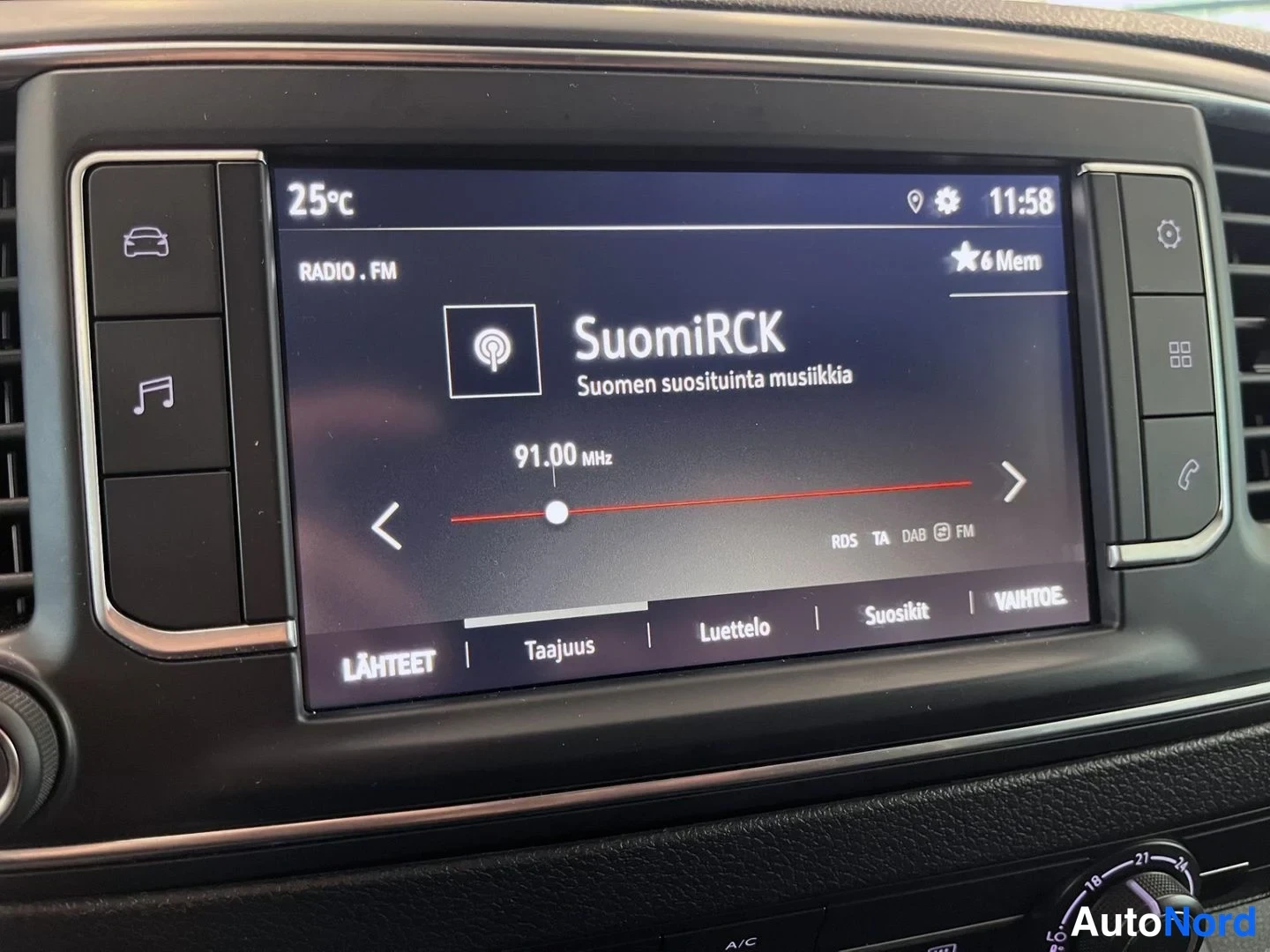 Yksityiskohta: Kojeistoon upotetun viihdejärjestelmän näyttö kuuntelee SuomiRCK-radioasemaa FM-taajuudella 91.00 MHz; näytön alareunassa valikot LÄHTEET, Taajuus, Luettelo, Su