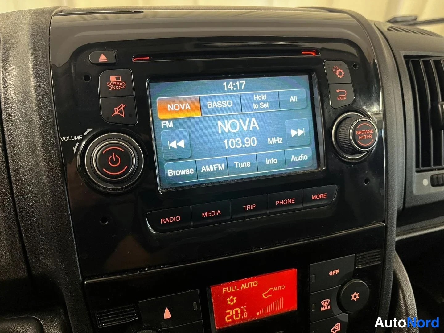 Muu: Kojelaudan keskikonsoli: radiopaneeli näyttää FM NOVA 103.90 MHz, kellonaika 14:17, alla FULL AUTO -ilmastointipaneeli asetuksella 20 °C.