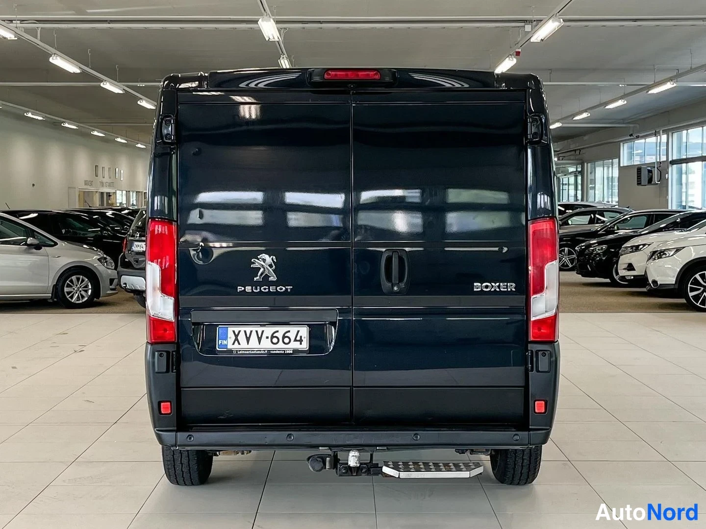 Takaa: Pakanäkymä tummasta Peugeot Boxer -pakettiautosta autonäyttelyssä; takaluukussa Peugeot- ja Boxer-tekstit, rekisterikilpi ja vetokoukku.