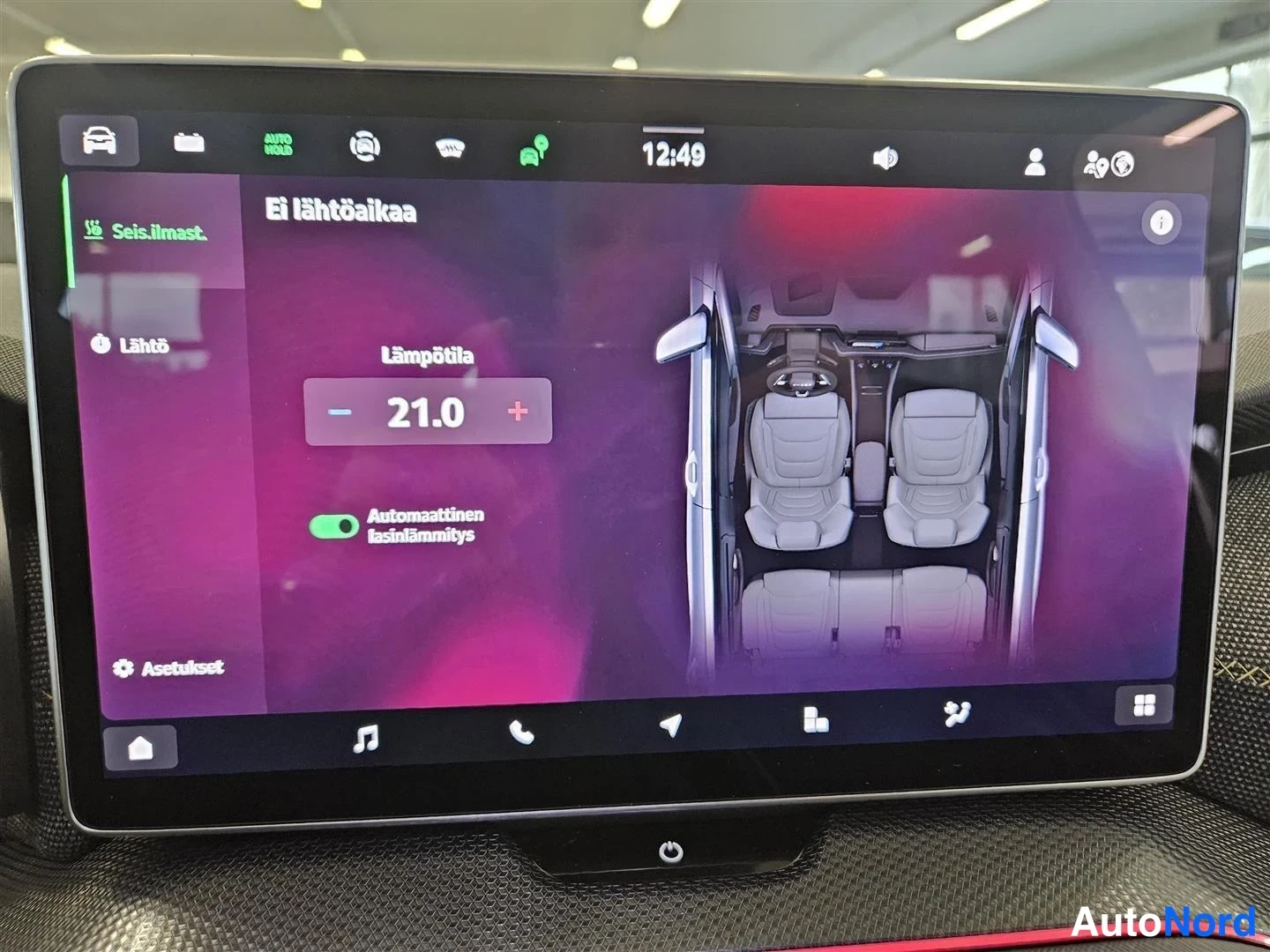 Edestä: Auton infotainment-näyttö Seis.ilmast. -valikossa: Lämpötila 21,0 astetta ja Automaattinen lasinlämmitys päällä, ei lähtöaikaa.