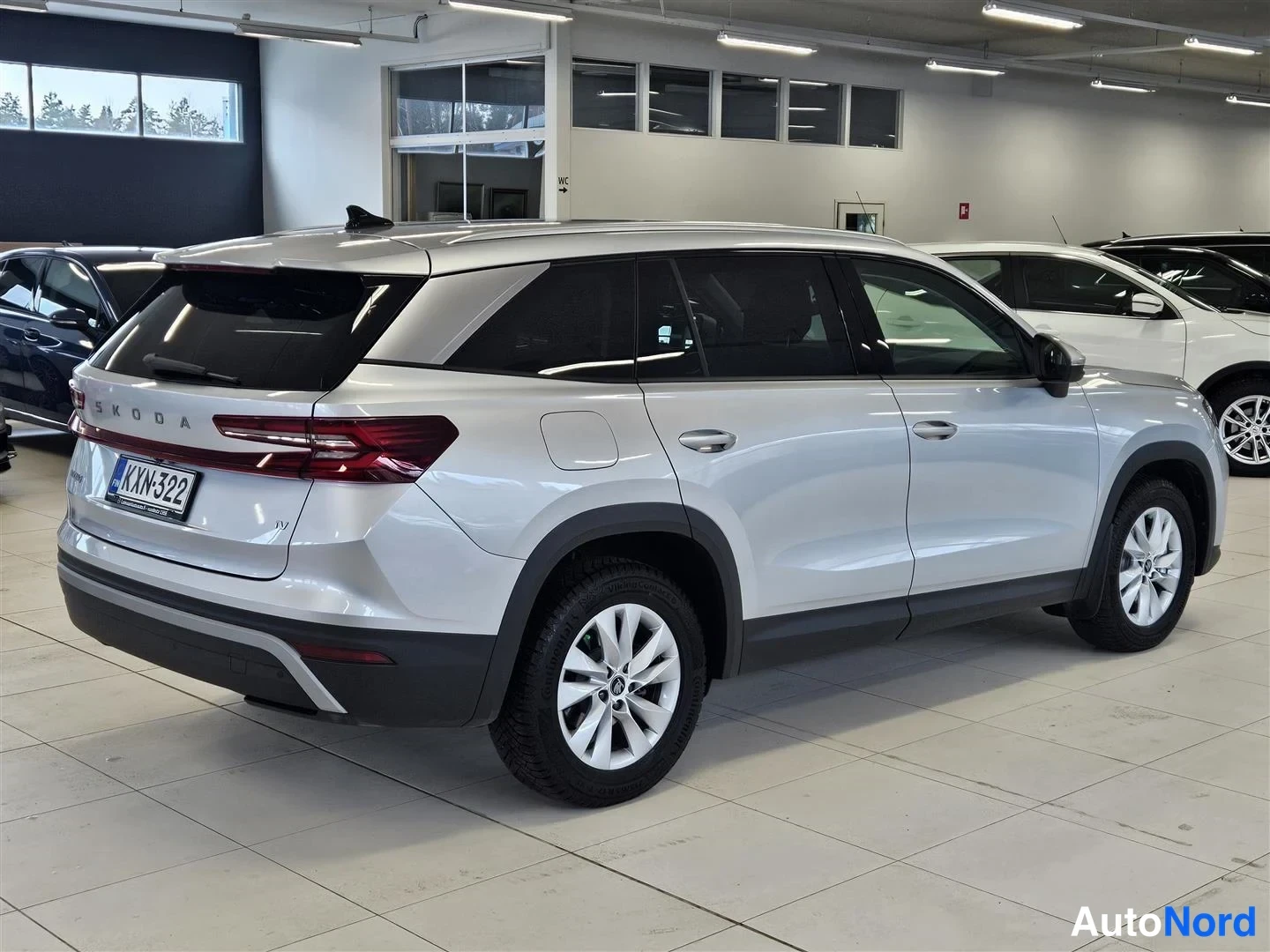 Takaviisto: Hopeanvärinen Škoda Kodiaq -maasturin takakulmanäkymä sisätiloissa, peräluukussa SKODA-teksti, rekisterikilpi.