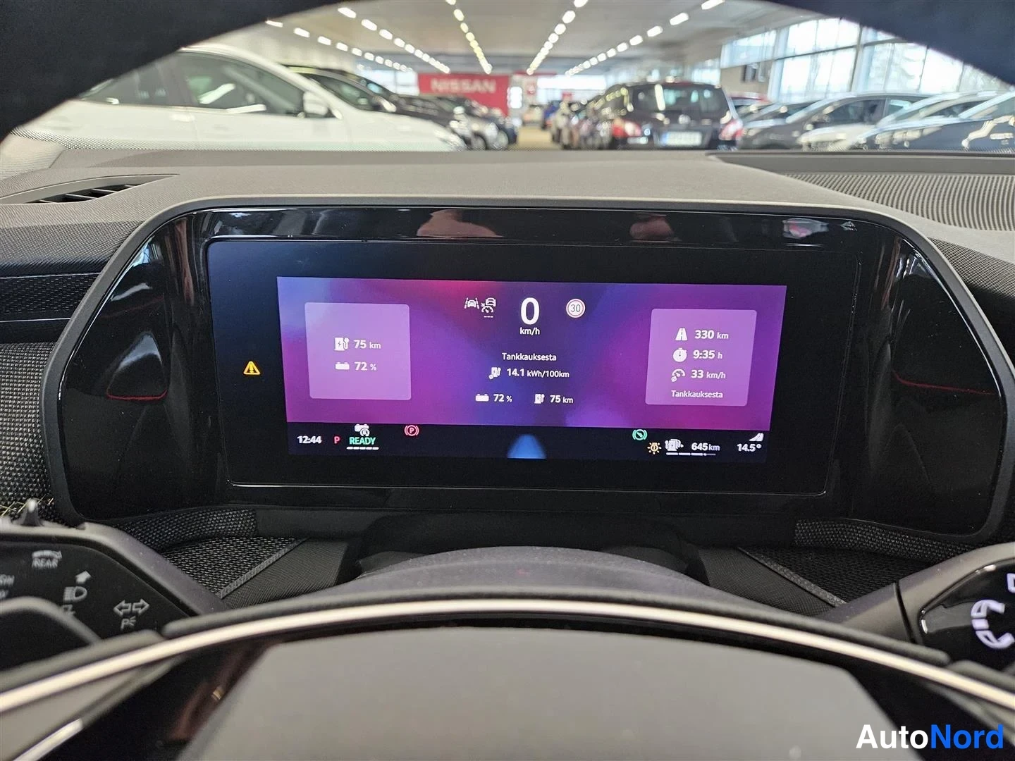 Muu: Sisäkuva: mittarinäytön aloitusnäkymä näyttää 0 km/h, 75 km sähköä, 72 % akun varausta, 14,1 kWh/100 km ja 330 km toimintamatkaa; taustalla autonäyttelyn autot.