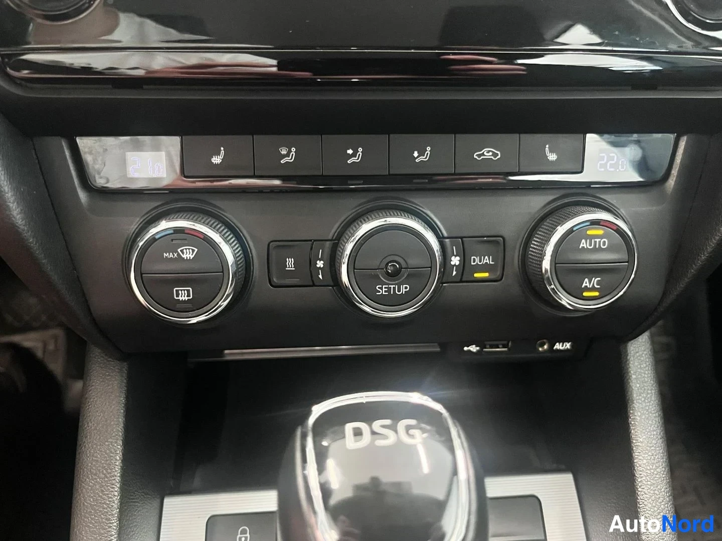 Yksityiskohta: Ilmastointipaneeli, jossa nappulat, AUTO ja A/C -merkit, DUAL-kytkin sekä DSG-merkitty vaihdekeksi. USB- ja AUX-portit näkyvät.