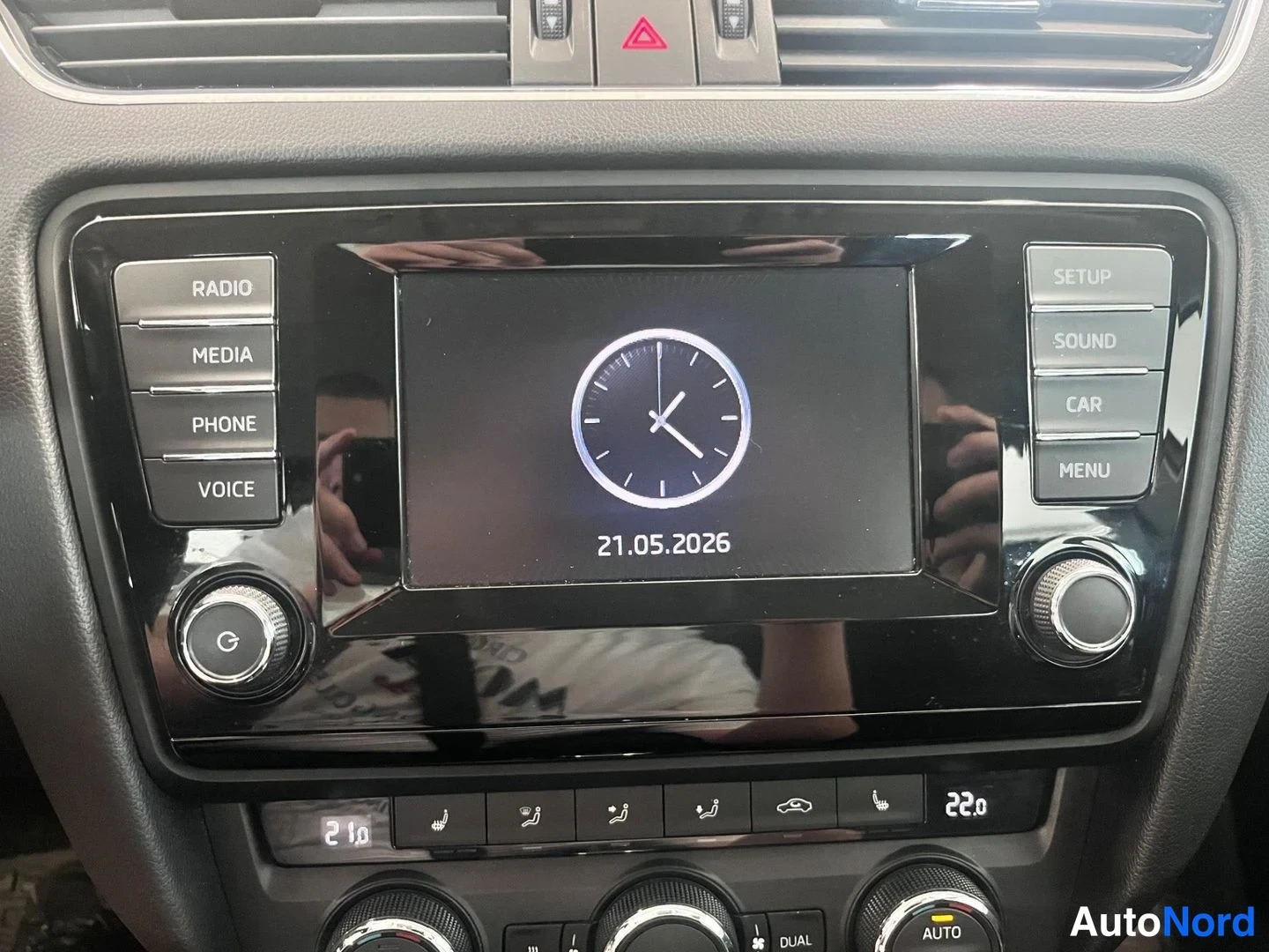 Yksityiskohta: Viihdejärjestelmän näyttö näyttää kellon ja päivämäärän 21.05.2026; paneelinapeissa RADIO, MEDIA, PHONE, VOICE, SETUP, SOUND, CAR, MENU.