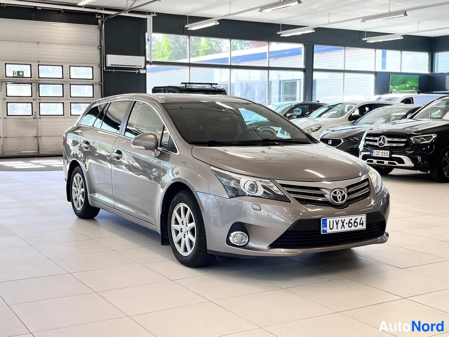 Etuviisto, nokka oikealle: Toyota Avensis -farmari etuviistosta oikealta, harmaanbeige värinen, rekisteritunnus.