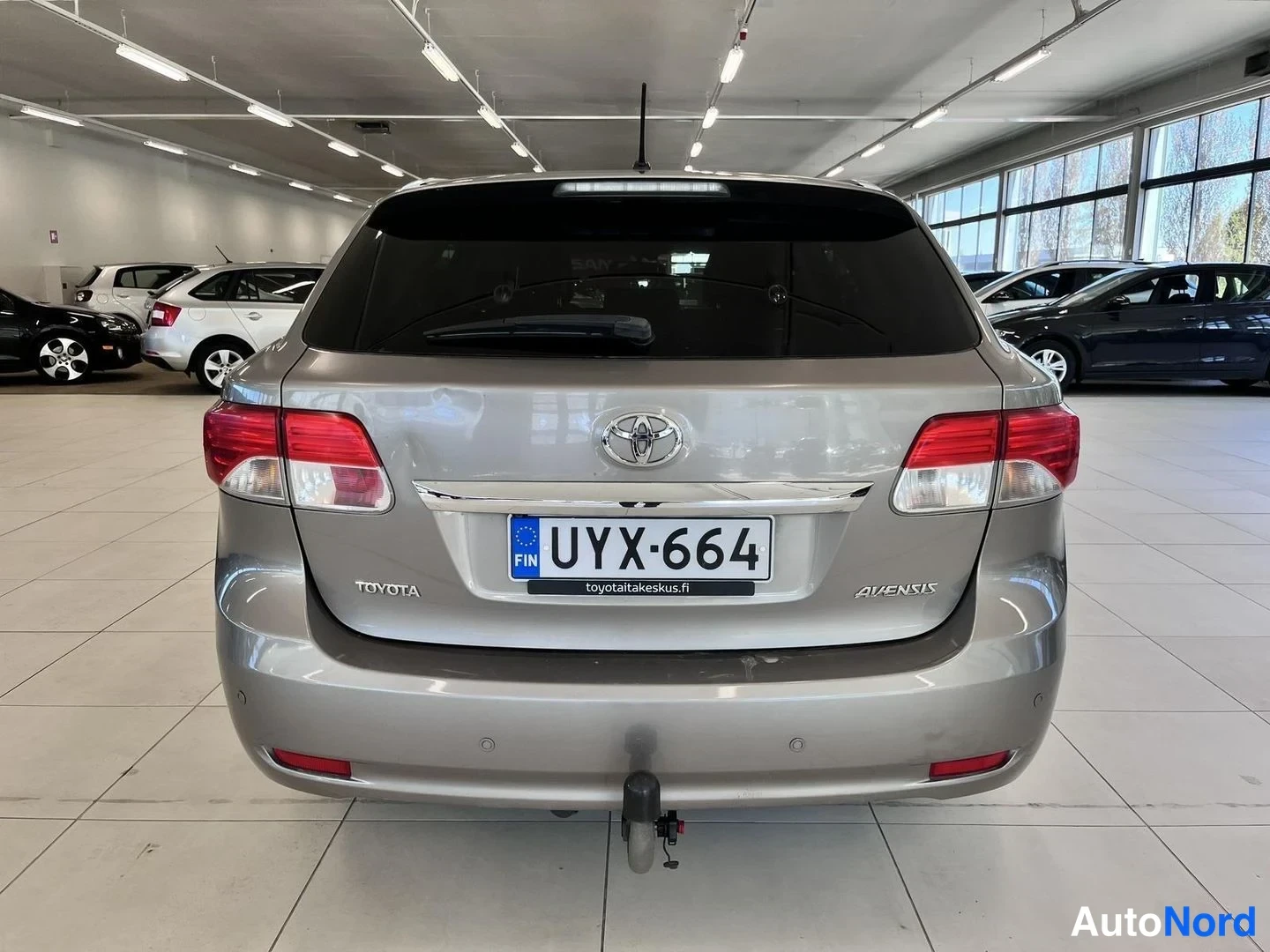 Takaa: Toyotan suora takanäkymä; rekisteri ja Avensis-merkintä näkyvät, taakse asennettu kytkinkoukku.
