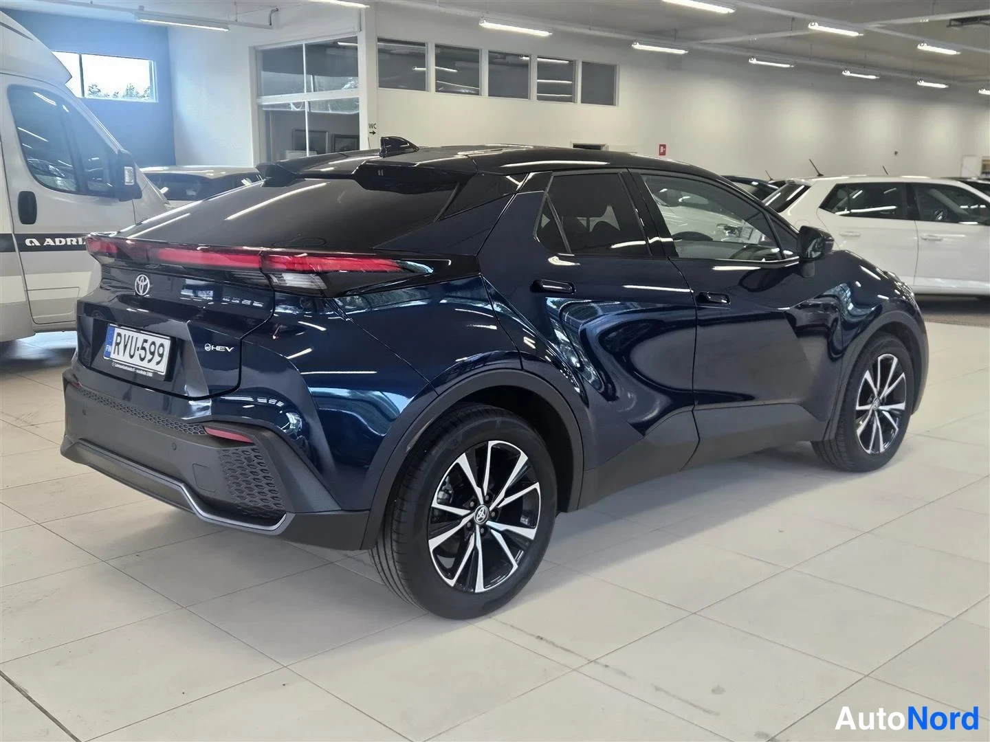 Takaviisto: Tummansininen Toyota C-HR Hybrid -maastoauton takaosa ja vasen kylki kuvattuna kolmannespäin sisätiloissa.