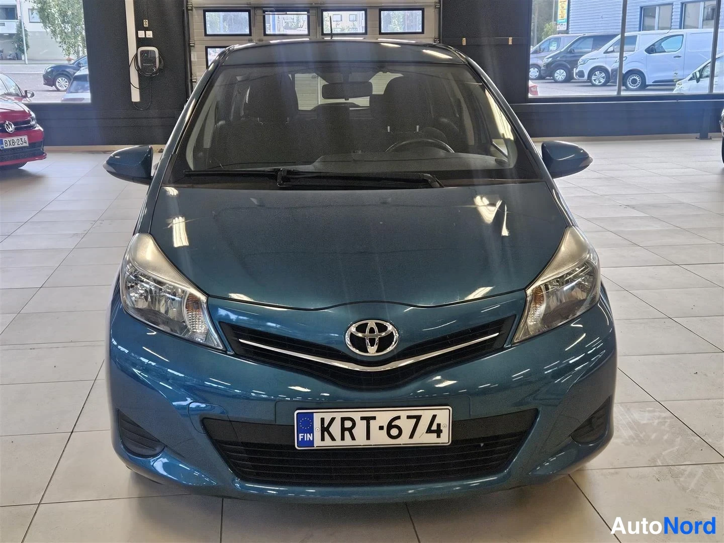Edestä: Toyota Yaris suoraan edestäpäin, sinivihreä kori, Toyota-merkki ja rekisteri keulassa.