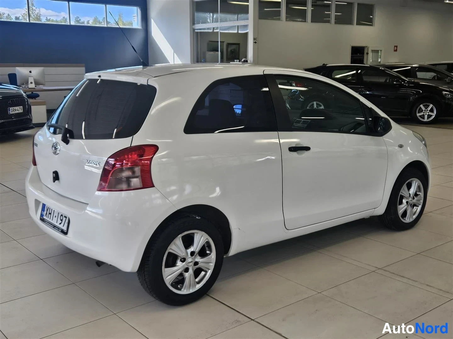 Takaviisto: Valkoisen Toyota Yaris -henkilöautin takakulma sisätiloissa, rekisteritunnus.