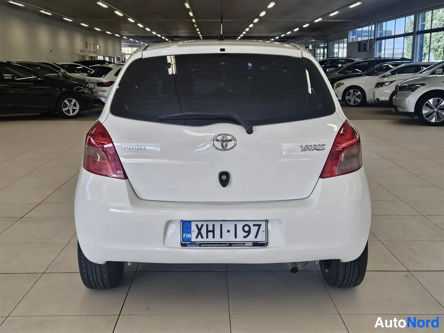 Takaa: Valkoisen Toyota Yarisin takaosa suoraan takaa, TOYOTA- ja YARIS-merkit sekä rekisteritunnus.