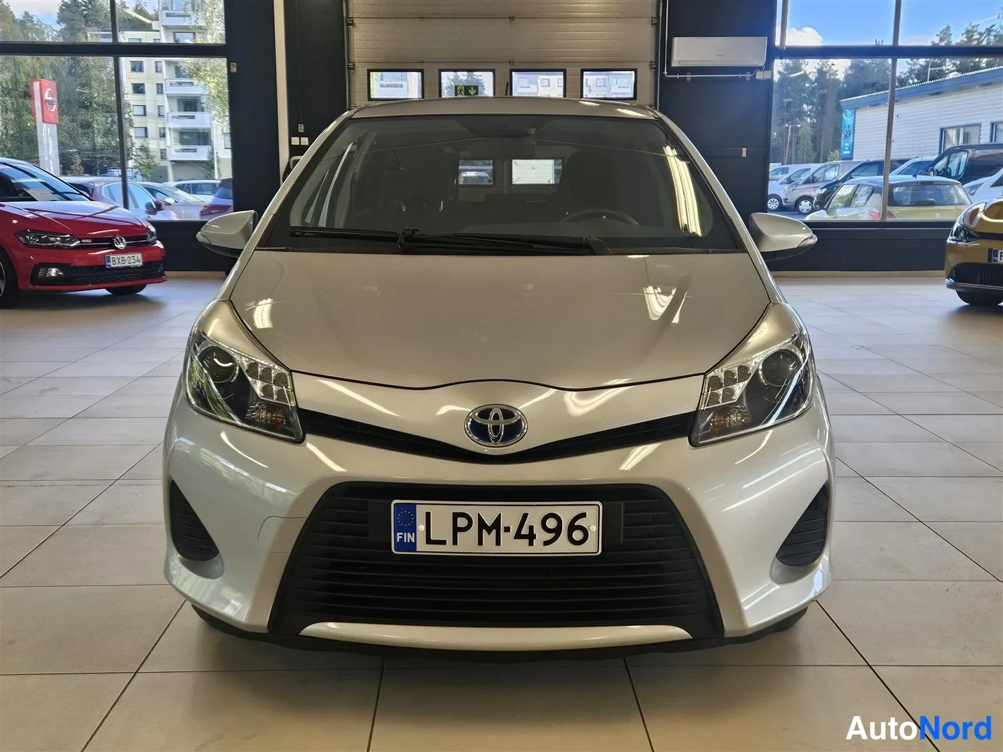 Edestä: Toyota Yaris suoraan edestä kuvattuna autosalissa, rekisteritunnus.