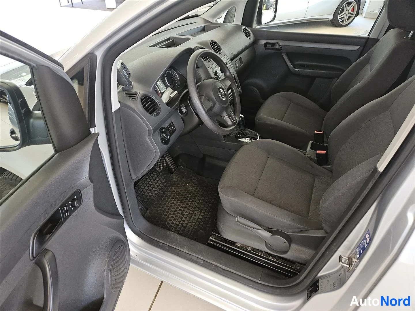 Muu: Auton etuosa sisätilat: kuljettajan ovi auki, harmaa kangasistuin, ratissa VW-logo, mittaristo ja matopohjamatto.