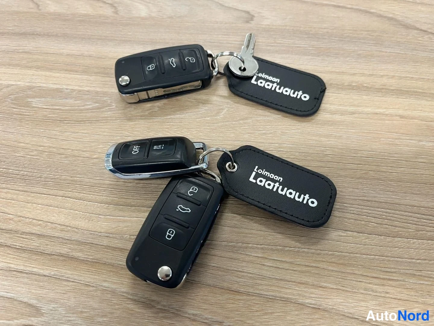Muu: Kaksi Volkswagen-avainnutta ja avain 'Loimaan Laatuauto'-avainnimillä puupöydällä.