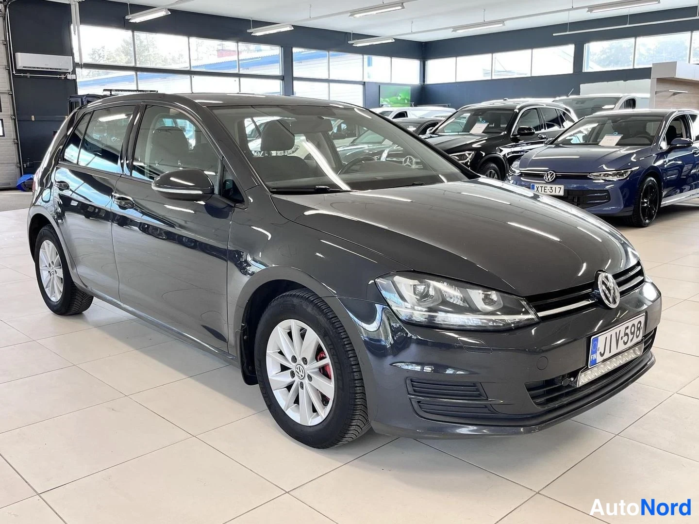 Etuviisto, nokka oikealle: Tummanharmaa viisiovinen hatchback etuviistosta oikealta showroomissa, rekisteritunnus, LED-nauha etupuskurissa.