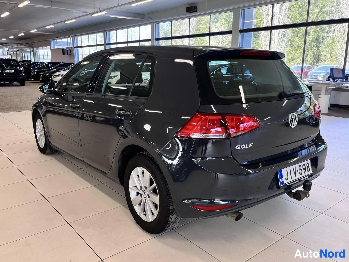 Takaviisto: Tummanharmaan Volkswagen Golfin vasen kylki ja takaosa vinosti kuvattuna; rekisteri ja vetokoukku näkyvät.