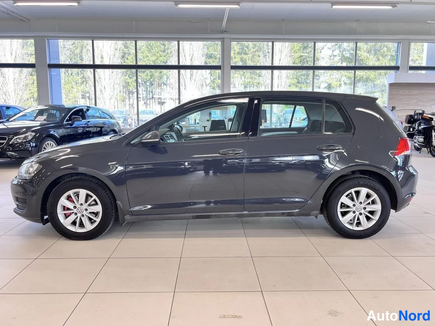 Sivulta: Tummanharmaan Volkswagen Golfin vasen kylki sivukuvassa neljästä ovesta ja hopeisista vanteista näkyvinä.