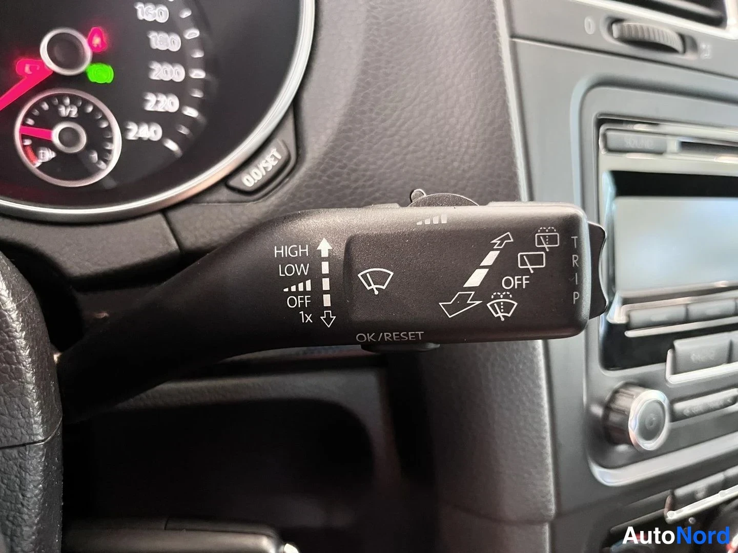 Yksityiskohta: Tuhkaluukun vipu kytkimineen: HIGH, LOW, OFF, 1x, OFF/RESET ja TRIP-merkit, taustalla osa nopeusmittarista ja radiosta.