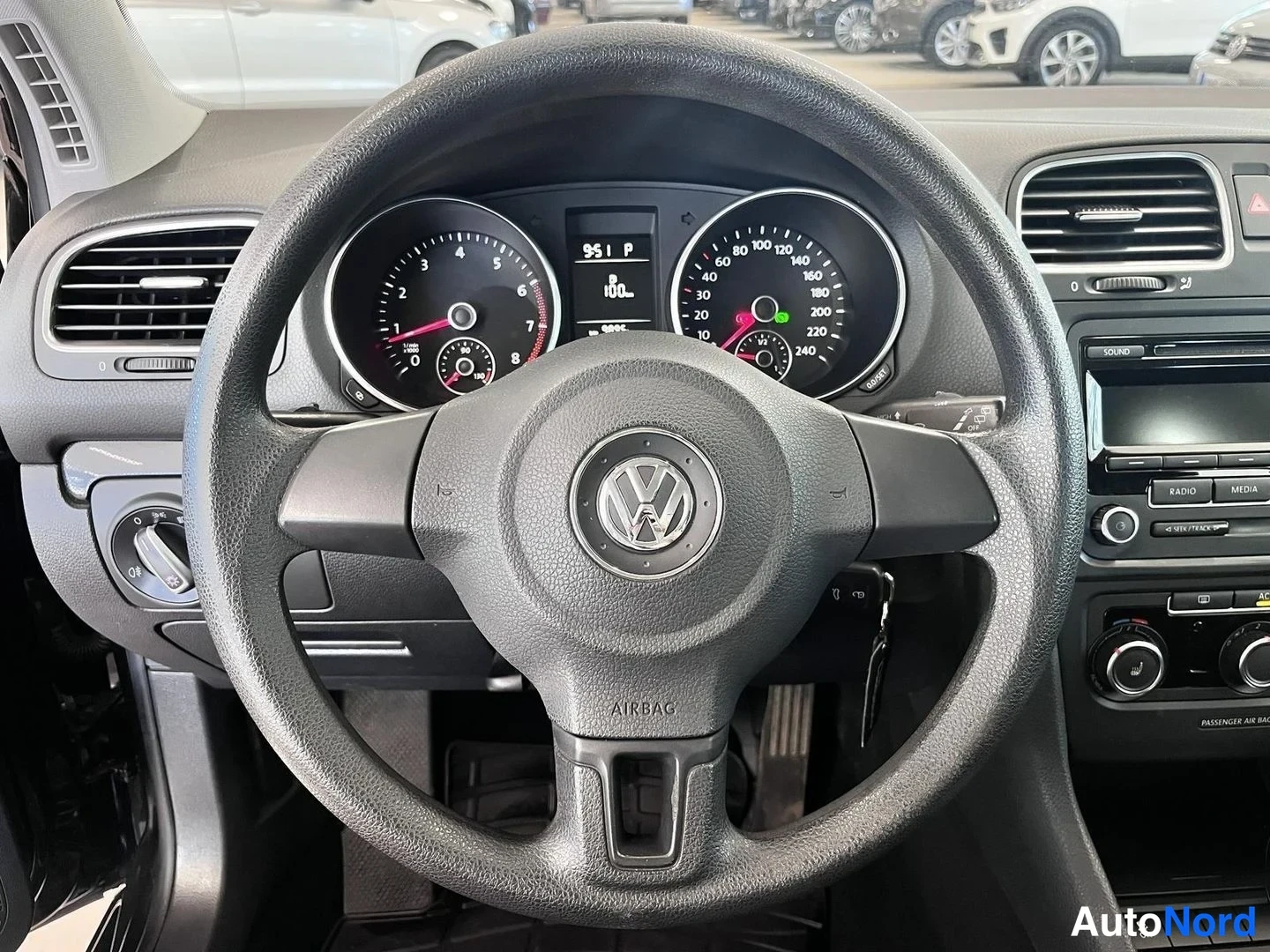 Yksityiskohta: Sisätilan kuva: kuljettajan näkökulmasta Volkswagen-ohjauspyörä ja taakse taulun taulut ovat ilmastointivetoa kohdassa P. Nyt 100 km, mittari lukema 187248 km.