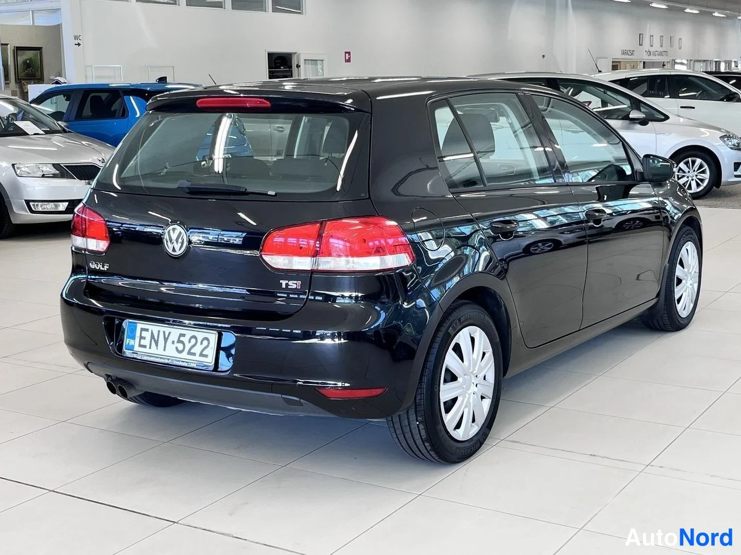 Takaviisto: Volkswagen Golf -viistoperä takaa oikealta kuvattuna; musta koripaneeli, takavalo, -rekisterikilpi ja valkoreunustettu pyörä autosalissa.