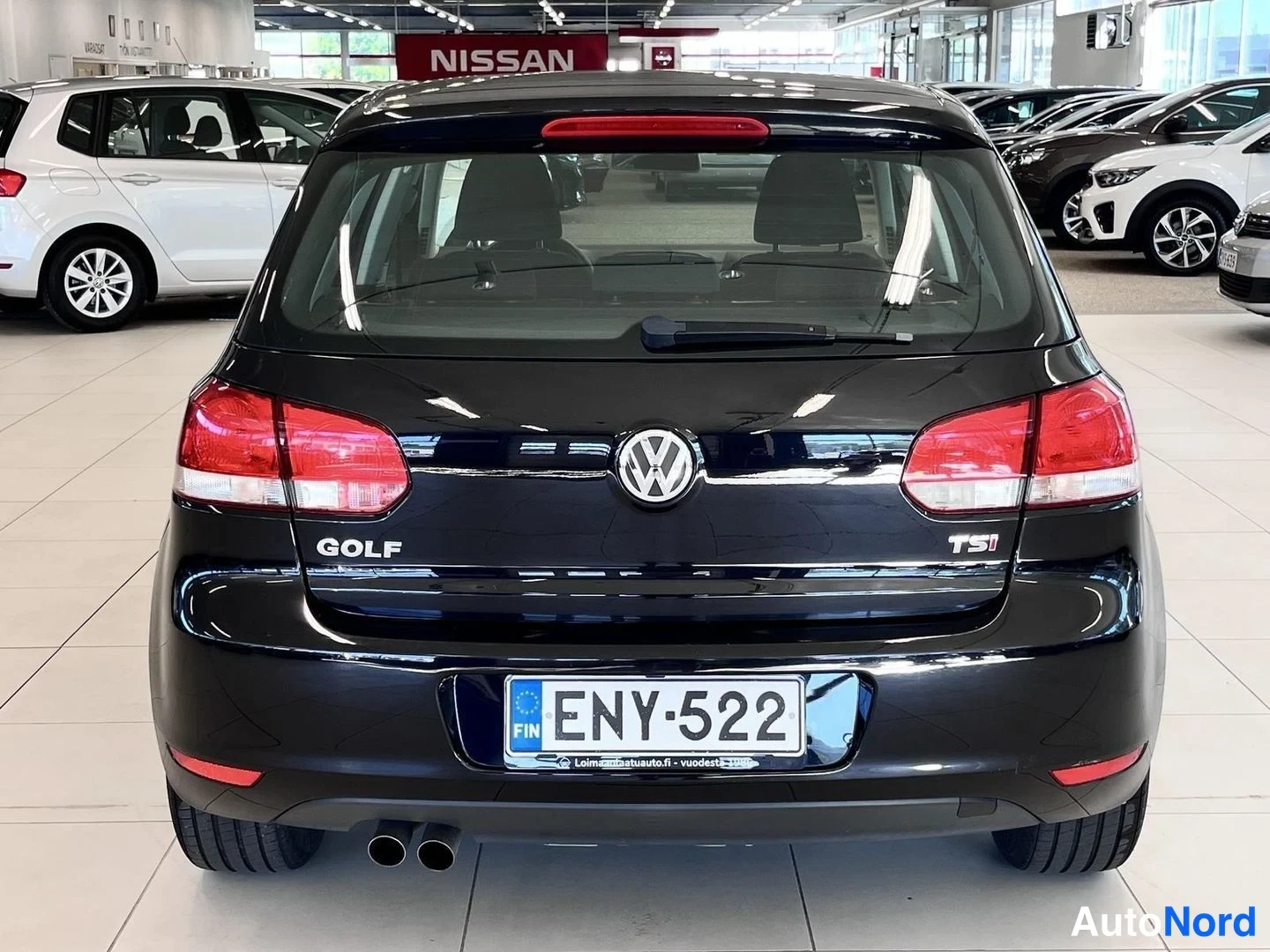 Takaa: Volkswagen Golf -viistoperän perä suoraan takaa: tumma koriväri, punaiset takavalot, GOLF- ja TSI-merkit, -kilpi ja kaksi pakoputkea autosalissa.