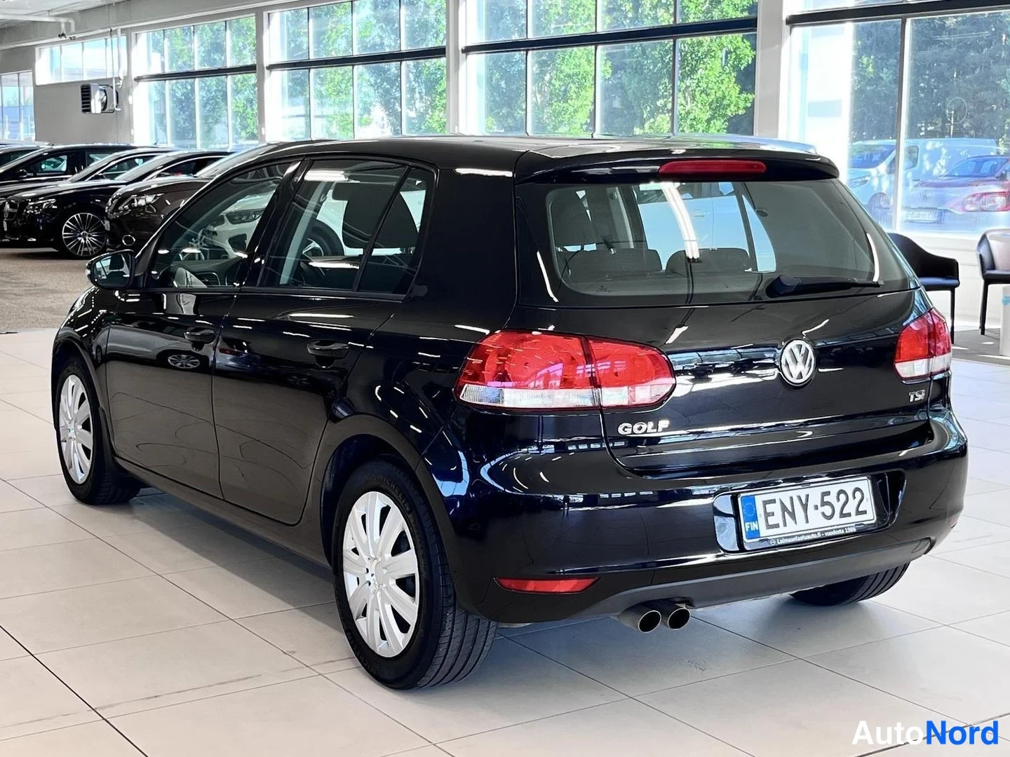 Takaviisto: Volkswagen Golf -viistoperä takaa vasemmalta kuvattuna; musta koripaneeli, takavalo, GOLF-merkki, -rekisterikilpi ja kaksoispakoputki valoisassa autosalissa.