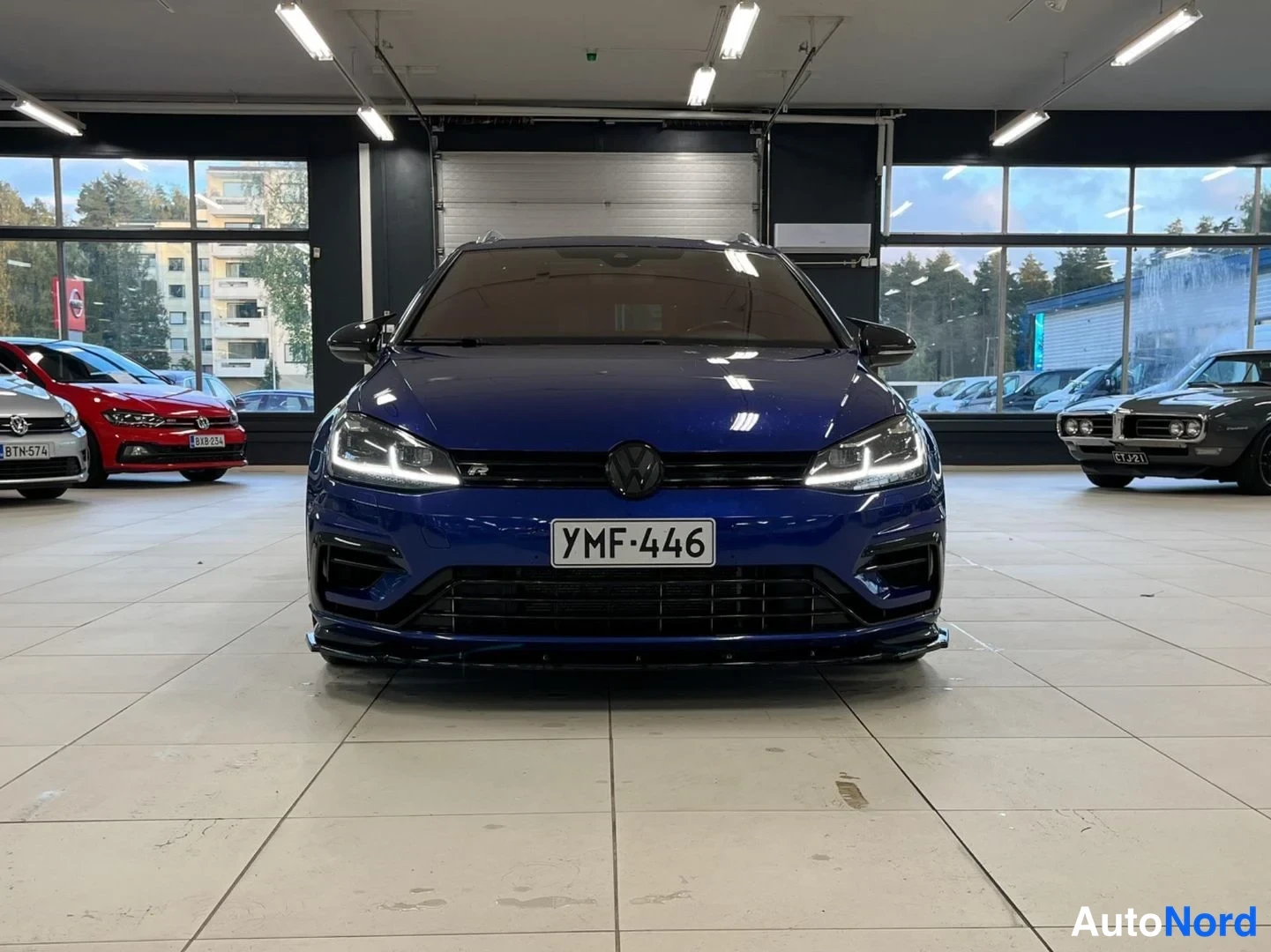Edestä: Sininen Volkswagenin farmarimallin etunäkymä showroomissa, rekisteritunnus, LED-ajovalot päällä ja musta etuspoileri.