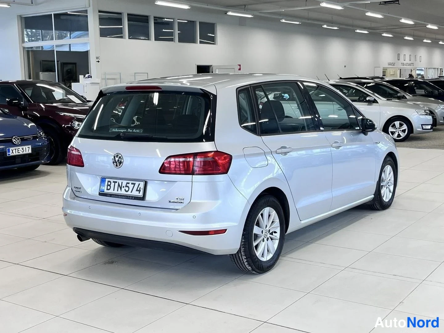 Takaviisto: Hopeanvärinen Volkswagen Golf Sportsvan takaviistosta autosalissa, rekisterikilpi.
