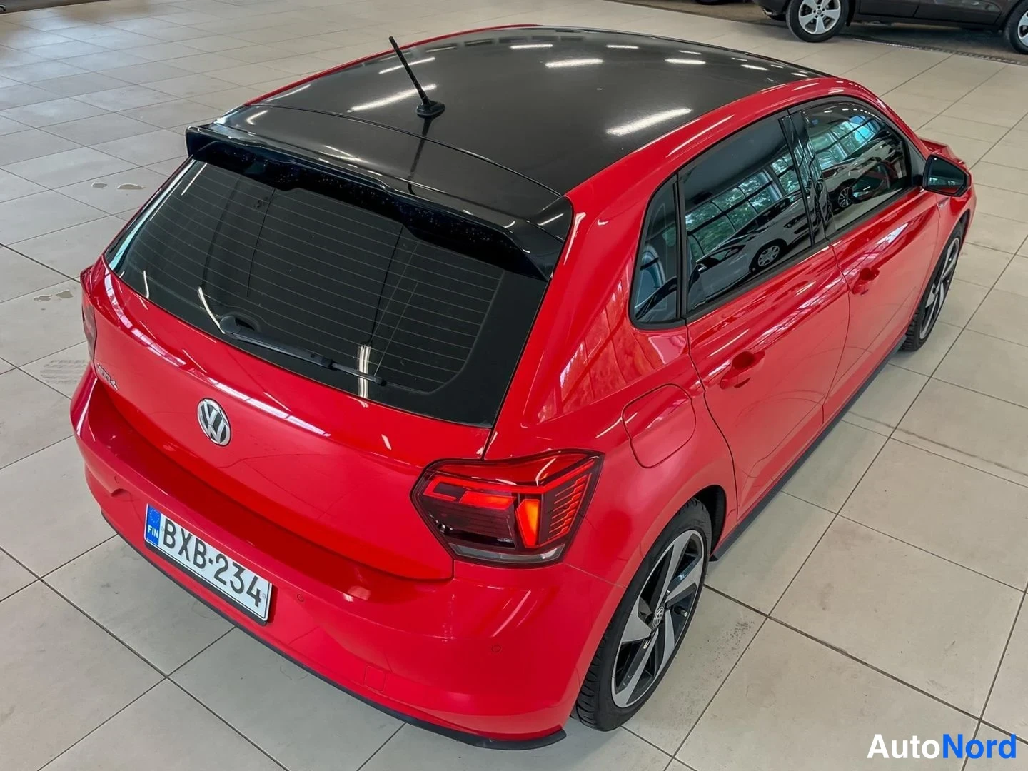 Takaviisto: Punainen Volkswagen Polo takaviistosta yläkulmasta, musta lasikatto ja takavalot näkyvissä.