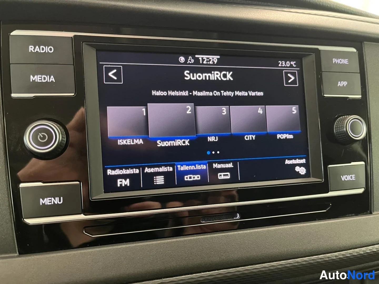 Yksityiskohta: Volkswagenin radioyksikön näyttö näyttää SuomiRCK-radiokanavaa kello 12:29 ja lämpötilan 23,0 °C; pienoiskuvissa muun muassa ISKELMA, NRJ, CITY ja POPfm, alareu