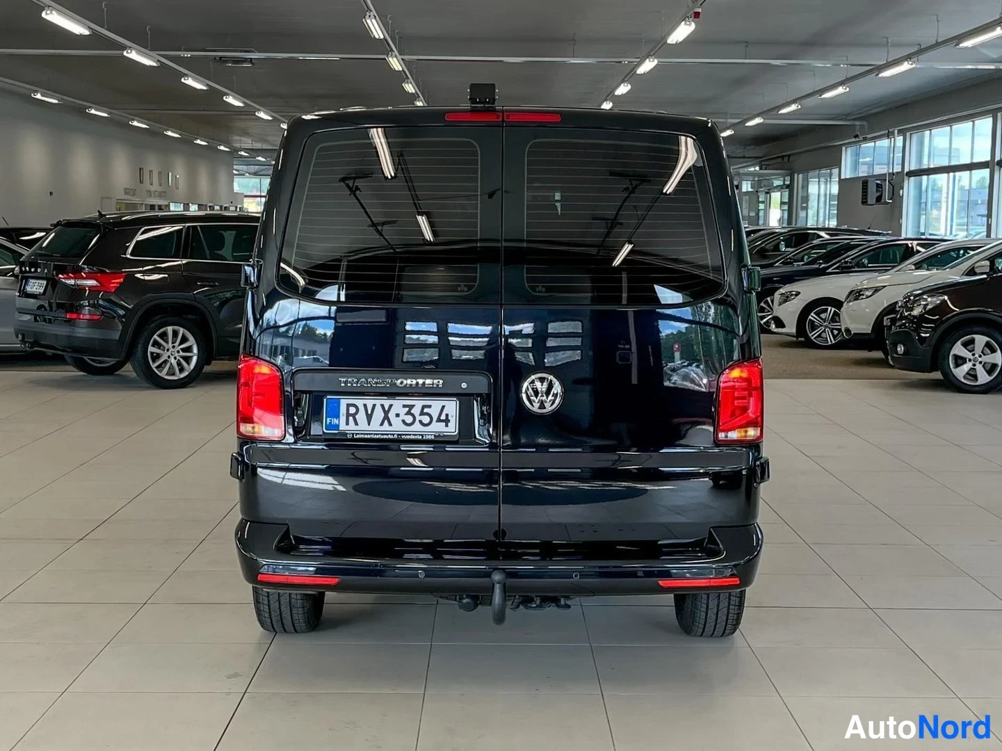 Takaa: Mustan pakettiauton takaosa suoraan takaa; rekisterikilpi, TRANSFER-teksti ja VW-merkki takaluukussa.