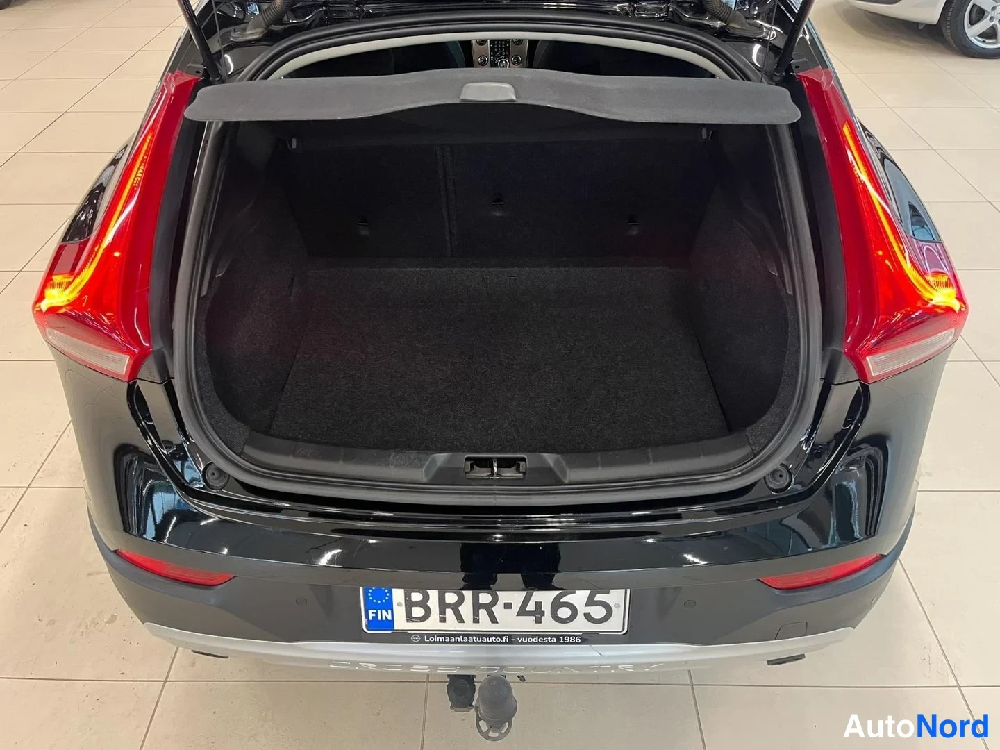 Takaa: Mustan Volvo V40:n avattu tavaratila hallissa; rekisteritunnus ja hinatakavin näkyvissä.