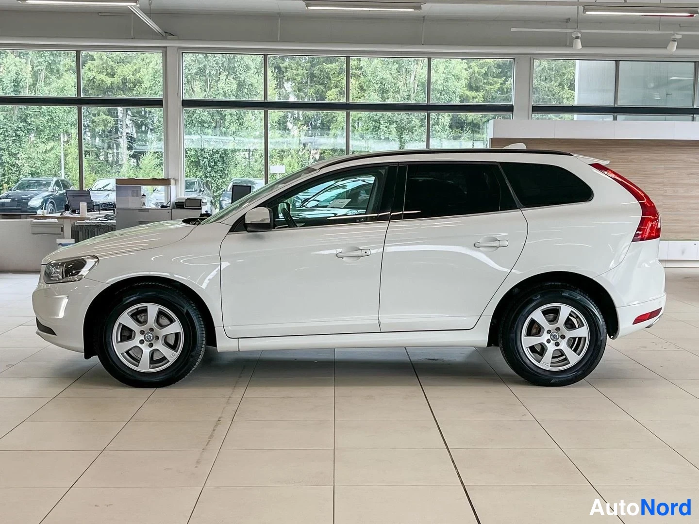 Sivulta: Valkoisen Volvo XC60:n kylkiprofiili autonäyttelyn salissa, oikea sivu kuvattuna.