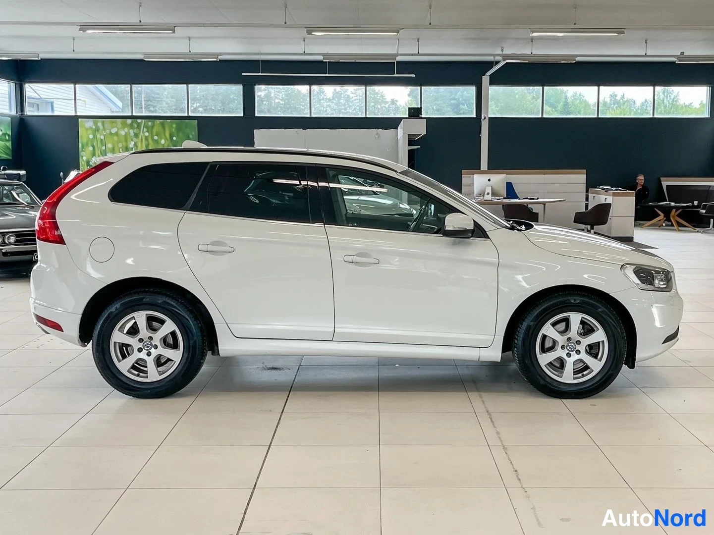 Sivulta: Valkoisen Volvo XC60:n kylkiprofiili autonäyttelytilassa, vasen sivu kuvattuna.