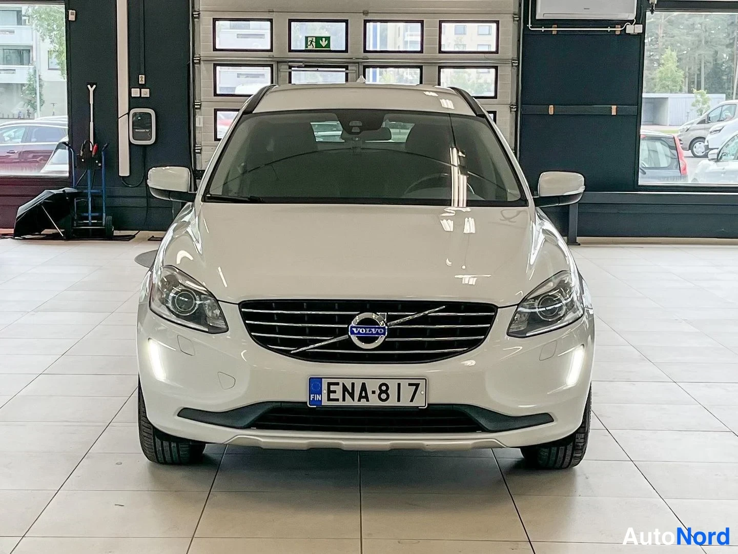 Edestä: Valkoinen Volvo XC60 suoraan edestä kuvattuna, Volvo-merkki maskissa ja rekisteritunnus.