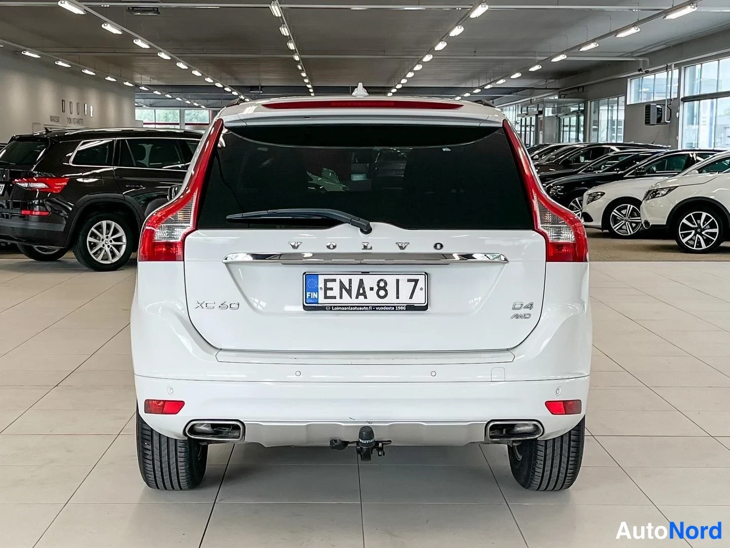 Takaa: Valkoisen tila-auton takaosan näkymä showroomissa; rekisterikilpi, XC60- ja D4 AWD -merkit, vetokoukku.