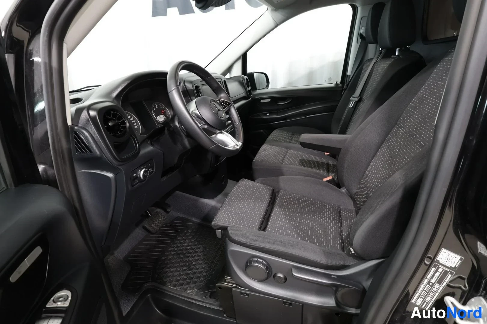 Muu: Sisätilakuva Mercedes-Benz Vito -pakettiauton etuosasta: ohjauspyörä, kojelauta ja tummat kankaisistuimet avonaisesta ovesta kuvattuna.