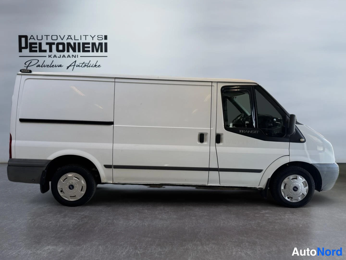 Sivulta: Valkoinen Ford Transit -pakettiauto sivusta sisätiloissa, Pitkä koritunnus TRANSIT ovessa.