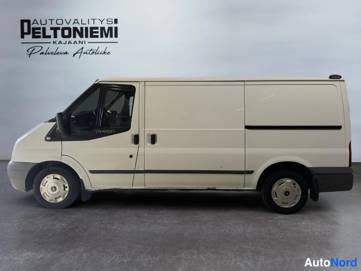 Sivulta: Fordonet on valkoinen Ford Transit -pakettiauto kuvattuna sivulta oikealta vasemmalle studio-hallissa.