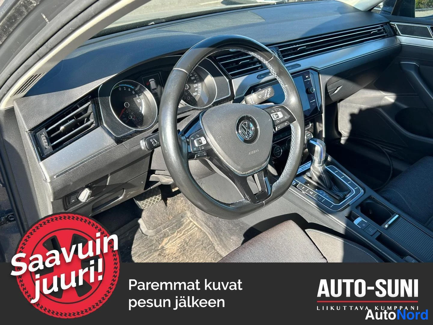 Muu: Auton ohjaamo: VW-merkillä varustettu ohjauspyörä, analogiset mittarit ja vaihteenvalitsin; matkalaukku tavaratilassa taustalla.