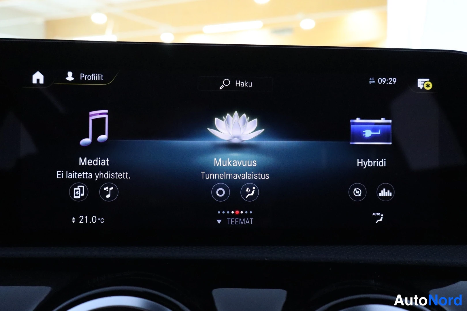 Muu: Auton infotainment-näyttö, jossa valikot Mediat, Mukavuus ja Hybridi; tunnelmavalaistuksen asetuksia ja 21,0 °C lämpötila näkyvät.
