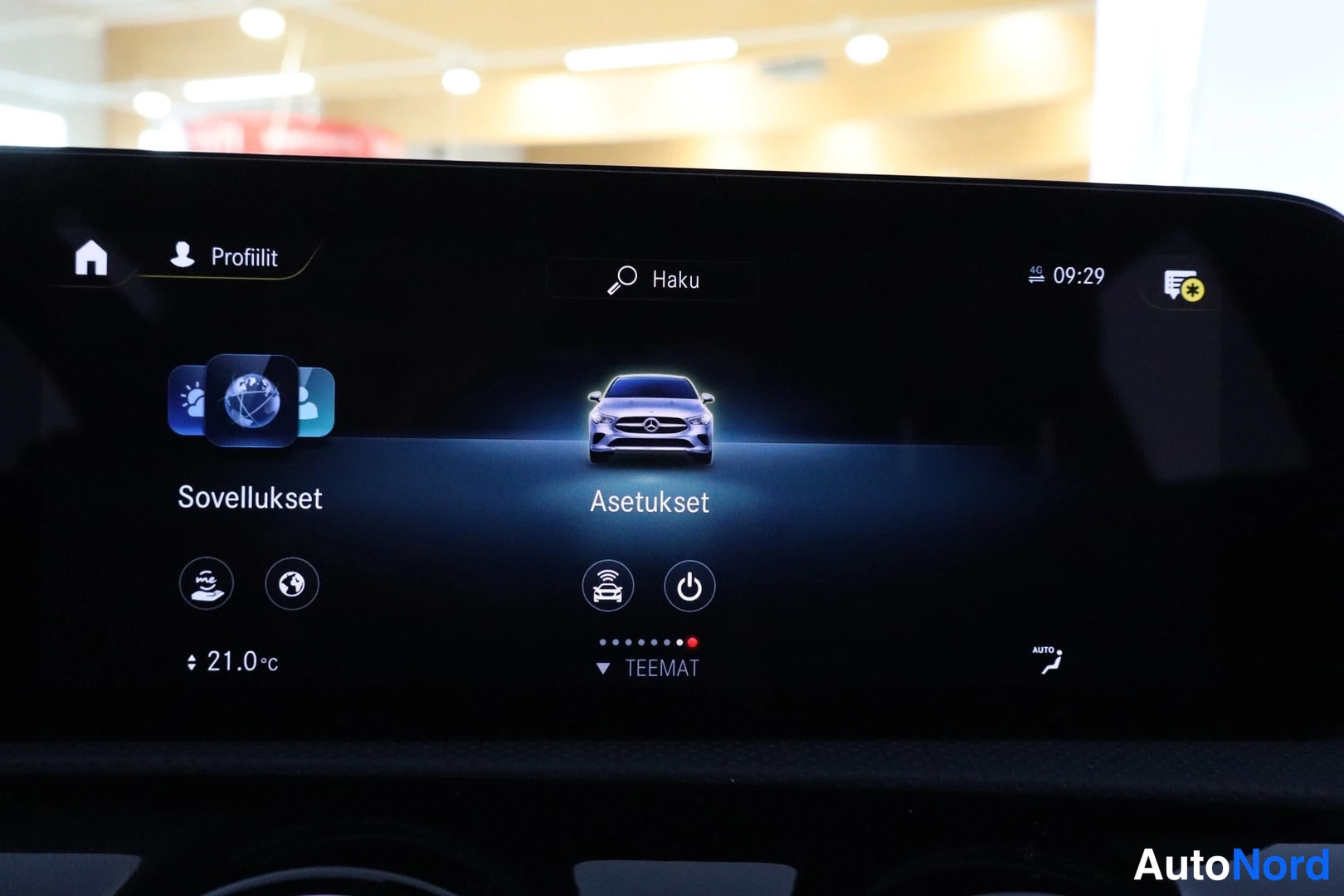 Muu: Auton infotainment-näytön Asetukset-valikko, jossa ovat Sovellukset ja asetuskuvakkeet; lämpötila 21,0 °C näkyy alareunassa.