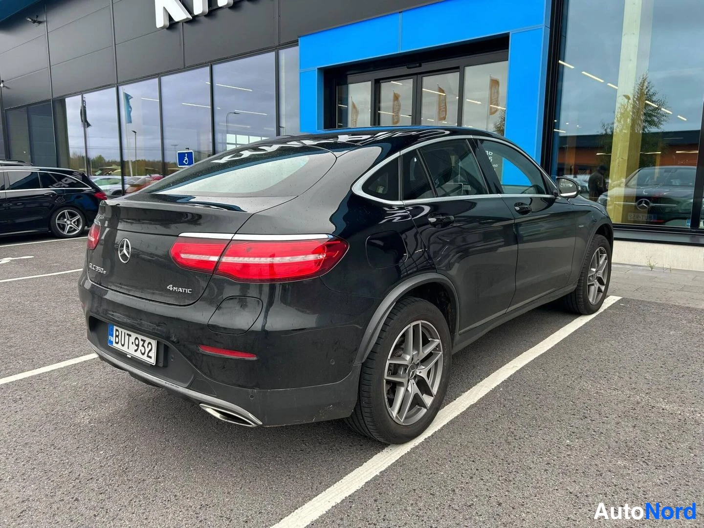 Takaviisto: Mustan Mercedes-Benz GLC Coupén takakulmanäkymä vasemmalta, takavalot ja rekisteritunnus näkyvät autoliikkeen edessä.