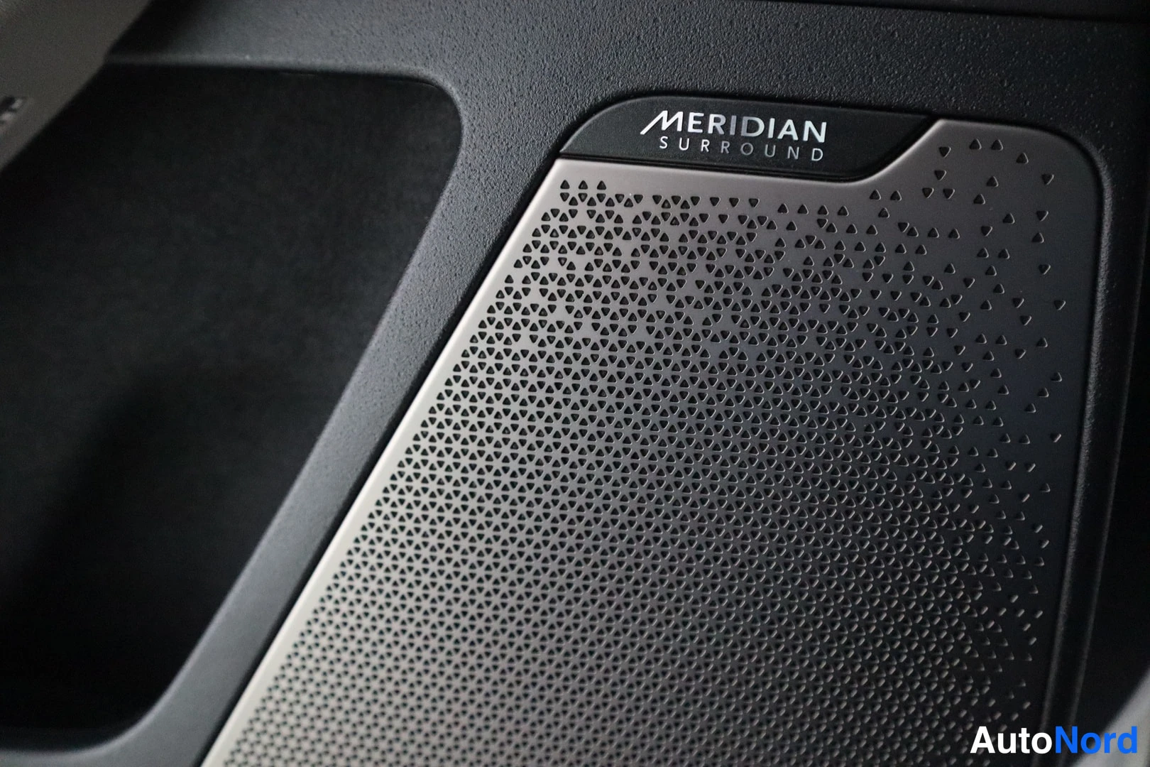 Muu: Takaoven sisäpaneelissa oleva Meridian Surround -kaiuttimen suojaverkko, jossa teksti 'MERIDIAN SURROUND'.