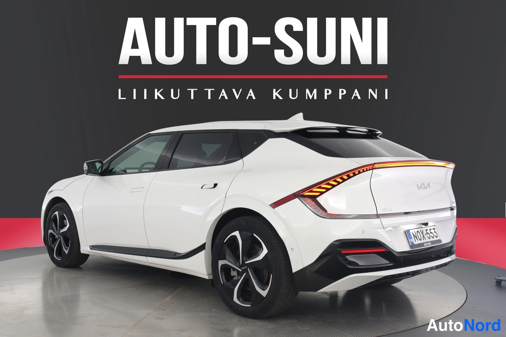 Takaa: Valkoinen Kia EV6 takaa sivusuunnasta, rekisteritunnus, takavalot syttyneenä.