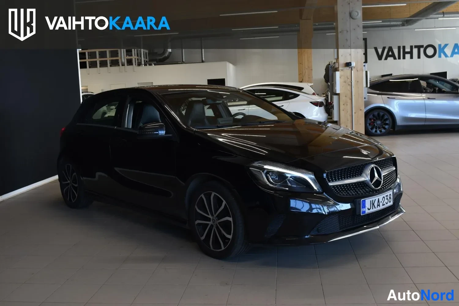 Etuviisto, nokka oikealle: Mercedes-Benz A 200 -viistoperä etuviistosta oikealle, musta kori ja -rekisterikilpi autosalissa.