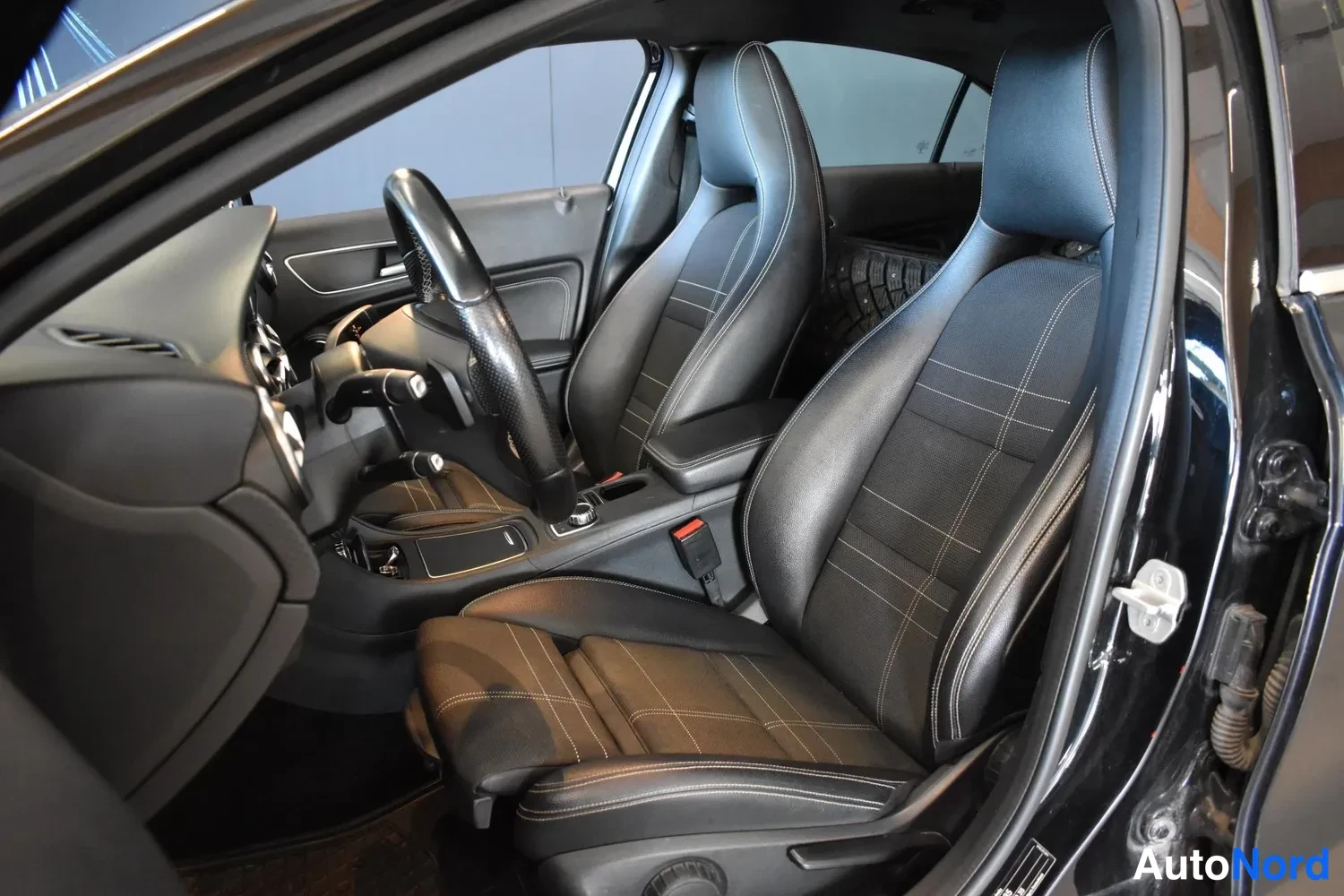 Sivulta: Mercedez-Benzin matkustamon etuistuimet ja ohjaamo kuvattuna avatusta etiovesta; mustat istuimet vaaleilla ompeleilla.