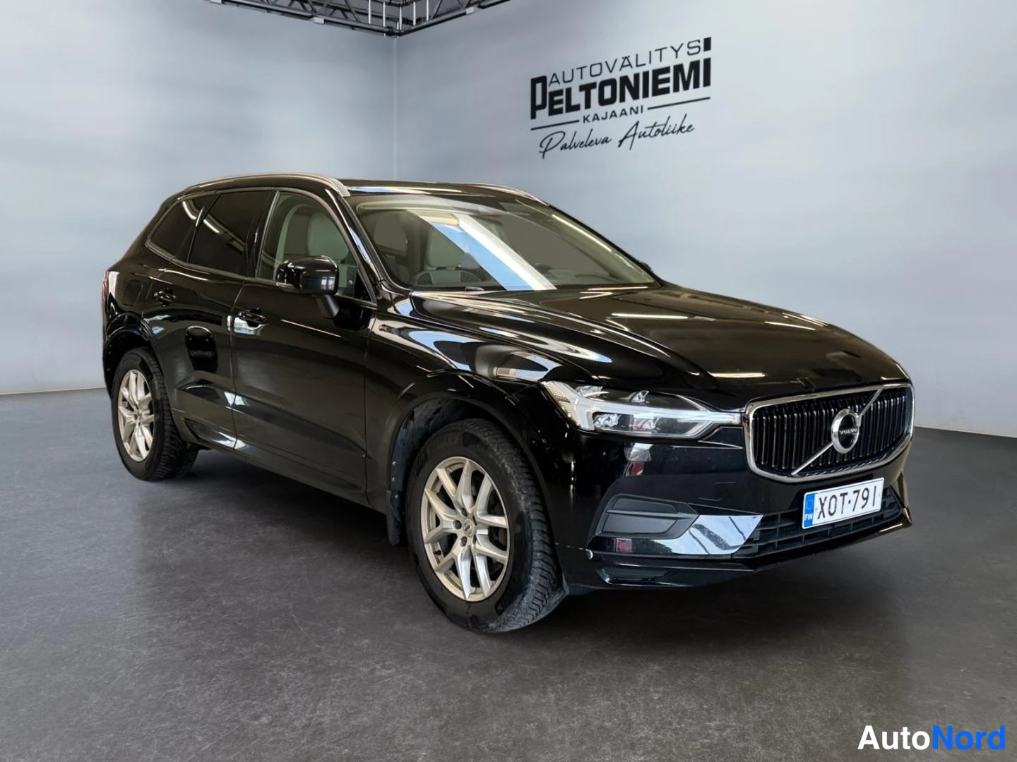Etuviisto, nokka oikealle: Musta Volvo XC60 -maasturi kulmatykistä edestä oikealta, rekisteritunnus,showroom-tilassa.