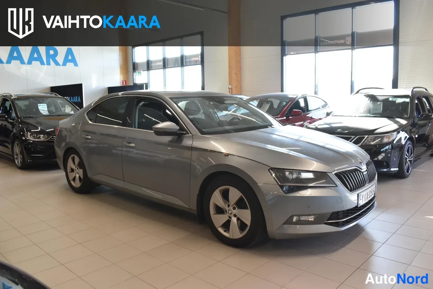 Etuviisto, nokka oikealle: Harmaan Skoda Superb -sedanin etukolmasosa oikealta edessä autonäyttelysalissa.