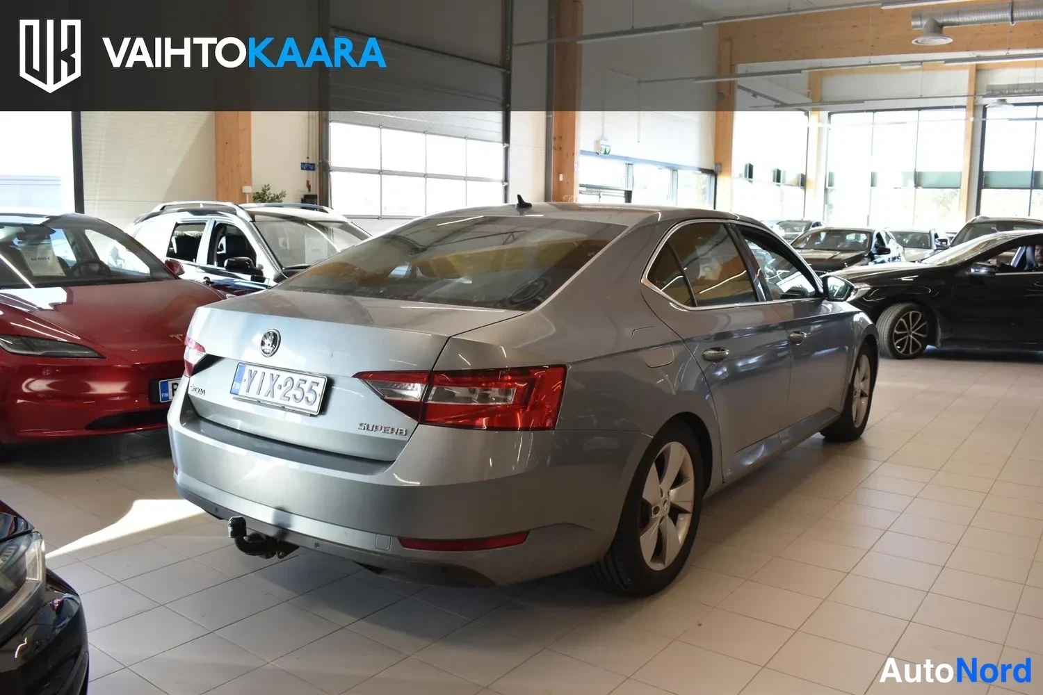 Takaviisto: Harmaan Skoda Superb -sedanin takaoltakulma oikealta; takana näkyy rekisteri ja takavilkut.